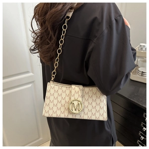Detalle de bolso bajo el brazo beige vintage con estampado de letras M y hebilla de oro