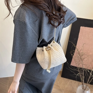 Chic beige woven bucket bag with pearl drawstring and gold chain worn on shoulder