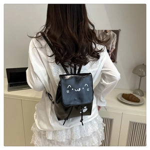 Detail of a black glossy mini cat backpack featuring cute white kitten paw prints