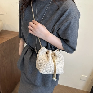 Beige woven bucket bag with gold chain and pearl drawstring on a model in a cozy setting