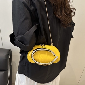 Glossy yellow leather pillow bag with C-shaped silver handle and gold chain strap on model