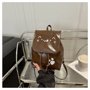 Detail of a brown patent leather mini backpack with a white cat face and paw print