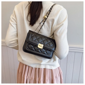 Detail of black quilted leather bag featuring gold wave buckle and chain strap