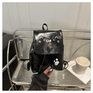 Detail of a black glossy mini backpack featuring a cute white cat face and paw prints