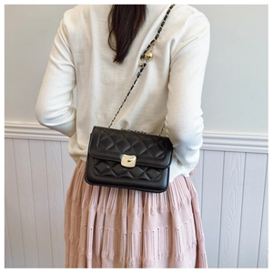 Detail of black quilted chain bag with gold ball adjuster worn by a model