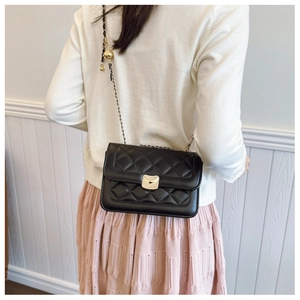 Detail of black quilted chain bag with gold metallic lock and adjustable orb pendant