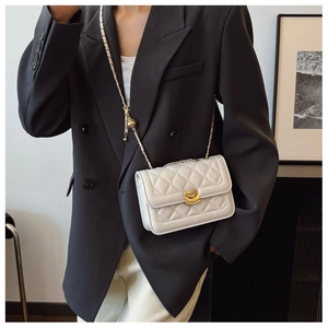 Close-up of a white quilted crossbody bag with gold hardware worn on a black blazer