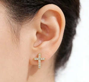 Close-up of a gold cross stud earring with micro-pave cubic zirconia on earlobe