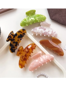 Six assorted large acetate hair claws with marble and tortoiseshell patterns in a tray