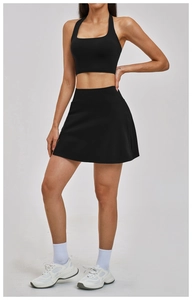 Front view of model wearing black halter sports top and high-waisted pleated tennis skirt