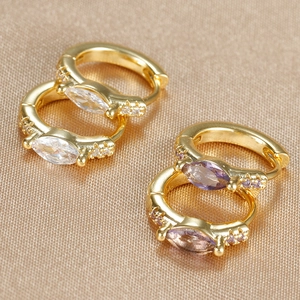 Macro shot of gold-plated hoop earrings with marquise-cut zircons on champagne satin