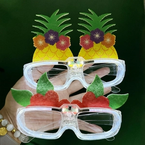 Close-up of LED glowing party glasses with pineapple and floral decorations on green background