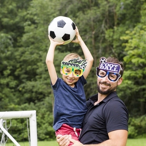 Father and son wearing festive soccer party glasses during outdoor sports activities