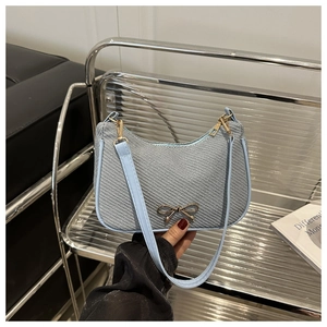 Close-up of light blue woven underarm bag featuring a golden bow metal accessory