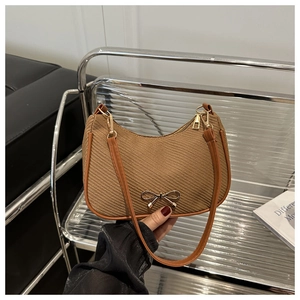 Detail of a brown woven shoulder bag featuring a golden metal bow fastener and leather trim