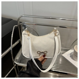 Close-up of a white woven texture shoulder bag with a gold bow metal clasp detail