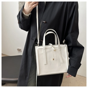 Detail of white glossy leather crossbody bag with metal accents and sleek square design