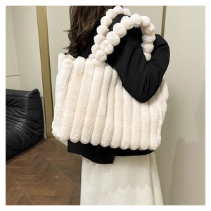 Detail of cream plush tote bag with vertical stripes and fluffy pom-pom handle strap