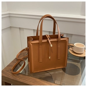 Detail of a brown leather tote bag showing golden hardware and drawstring on a wooden table