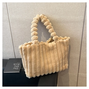 Detail view of the plush beige tote bag with a unique fuzzy ball handle and striped texture