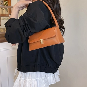 Minimalist caramel baguette shoulder bag with gold clasp shown on a model