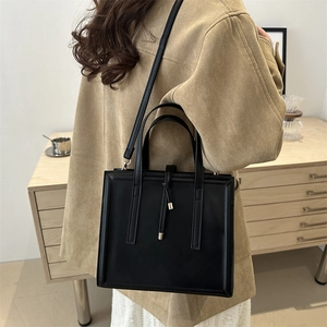 Minimalist black square tote bag with knot tassel detail shown on model in cozy interior
