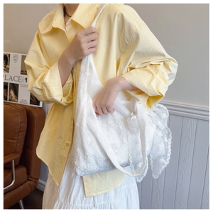 Close-up of a white floral lace tote bag with bow detail held by a model in a yellow shirt