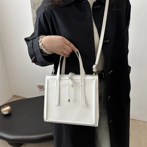 Elegant white faux leather tote bag with tassel detail and adjustable shoulder strap