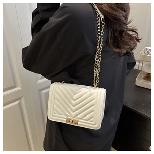Detail of white quilted chain bag with gold twist lock on shoulder of a woman