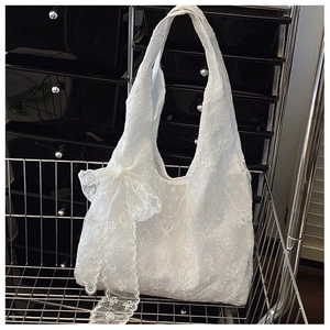 Detailed view of a white lace embroidered tote bag with a large decorative bow on a metal rack