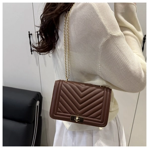 Detail of dark brown quilted chain bag with V-shaped stitching and gold square lock