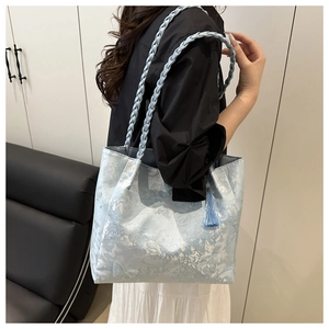 Detail of light blue floral textured tote bag with braided handle and tassel charm