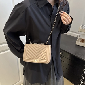 Quilted chevron beige crossbody bag with gold chain strap worn by a model