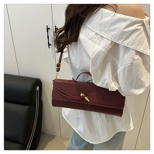 Detail of burgundy crocodile-embossed baguette bag with golden metal buckle clasp