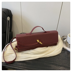 Close-up of burgundy crocodile pattern baguette bag featuring a gold knotted clasp and leather texture