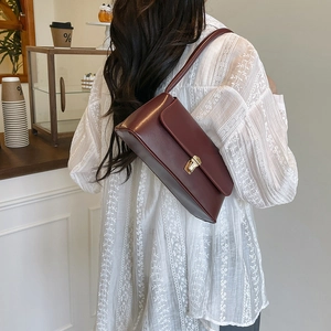 Minimalist burgundy baguette shoulder bag with gold metal buckle in a cafe setting