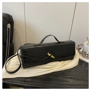 Detail of glossy crocodile pattern texture and golden knot buckle on black baguette bag