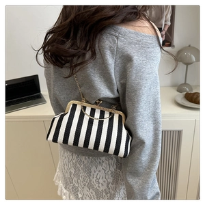 Gros plan d'un sac à fermoir baiser rayé noir et blanc avec chaîne dorée et texture tissée