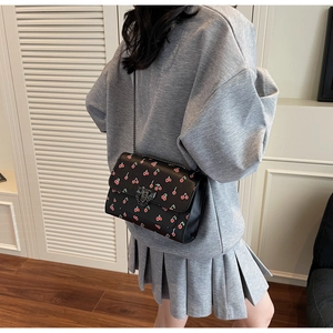 Détail d'un sac à bandoulière en cuir noir avec imprimé cerise et chaîne fine