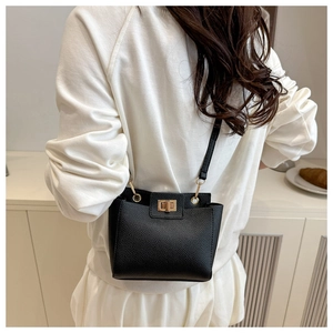 Sac à bandoulière noir à motif litchi avec fermoir doré porté par un mannequin en décor