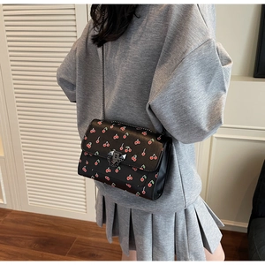 Vue latérale du petit sac bandoulière noir avec imprimé cerises et chaîne en métal