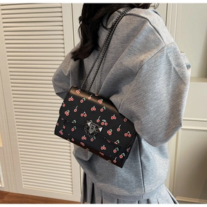 Détail d'un sac à bandoulière en cuir noir avec motifs cerises et fermoir en métal clouté