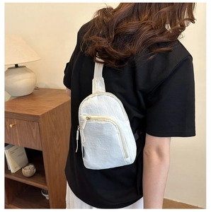 Detalle de una riñonera minimalista blanco crema llevada por una modelo en un interior