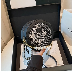 Detail of round black bag featuring white embroidery and luxury pearl chain strap