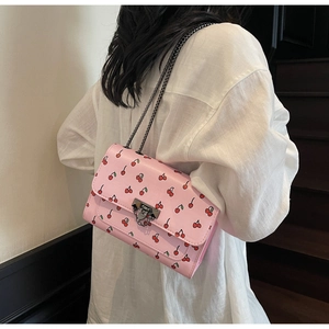 Détail du sac bandoulière rose à motif cerises avec chaîne porté par un mannequin