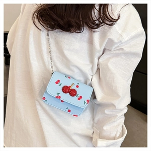Detail of light blue crossbody bag featuring red cherry prints and a jeweled cherry clasp