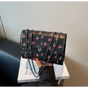 Détail du petit sac carré noir avec imprimé cerises et bandoulière chaîne