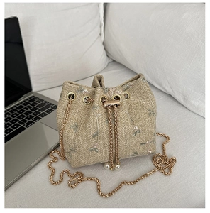 Detail of floral embroidery on a woven bucket bag with pearl chain straps on a bed