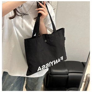 Detail of black nylon tote bag with white lettering and metal buckle on long shoulder strap