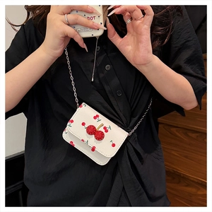 Close-up of white crossbody bag with red cherry print and 3D cherry charm on silver chain